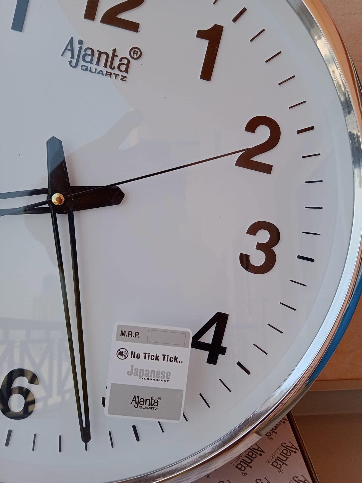  ساعة الحائط من أجانتا كوارتز. تتميز الساعة بمينا أبيض وإطار فضي أنيق يجمع بين التصميم العصري والأداء الموثوق. تعمل بتقنية الكوارتز لضمان دقة عالية في الوقت، كما أن الأرقام الواضحة تسهّل قراءتها من أي مسافة.