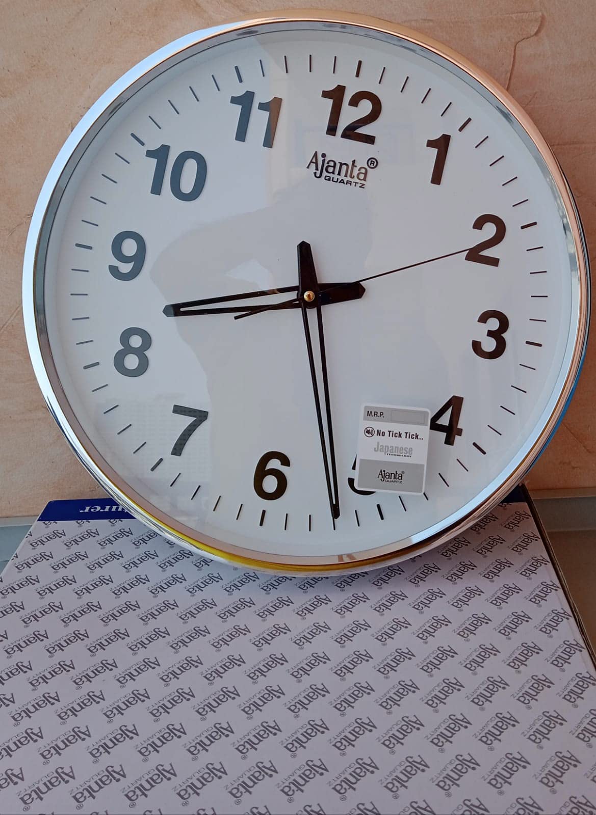  ساعة الحائط من أجانتا كوارتز. تتميز الساعة بمينا أبيض وإطار فضي أنيق يجمع بين التصميم العصري والأداء الموثوق. تعمل بتقنية الكوارتز لضمان دقة عالية في الوقت، كما أن الأرقام الواضحة تسهّل قراءتها من أي مسافة.