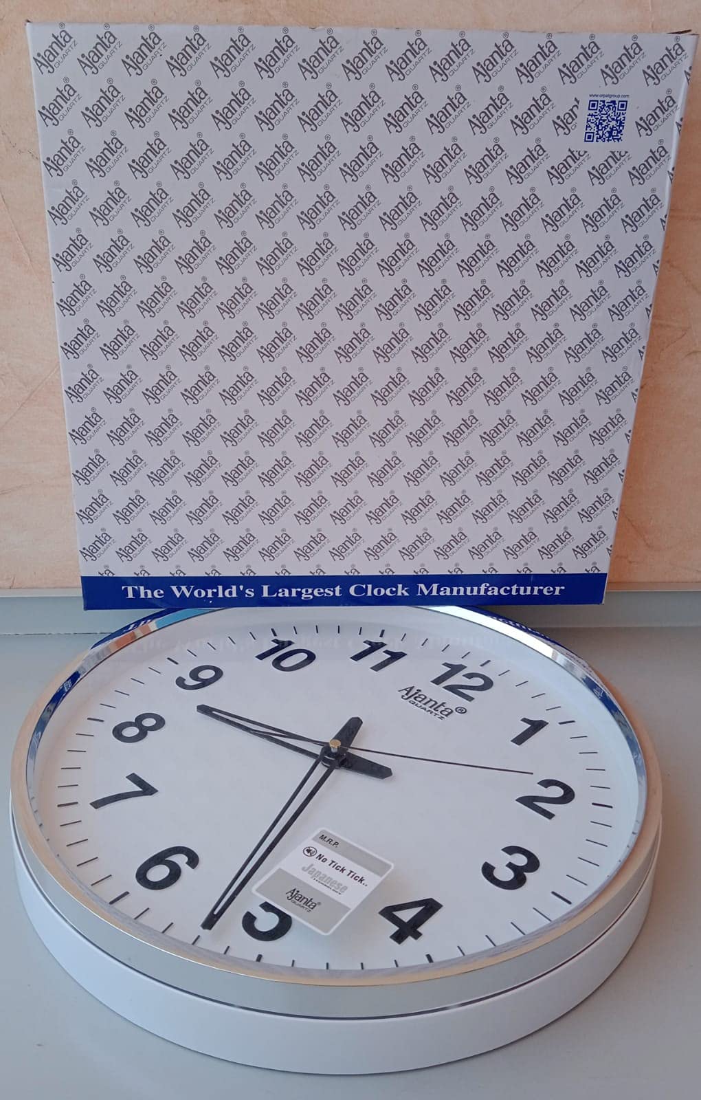  ساعة الحائط من أجانتا كوارتز. تتميز الساعة بمينا أبيض وإطار فضي أنيق يجمع بين التصميم العصري والأداء الموثوق. تعمل بتقنية الكوارتز لضمان دقة عالية في الوقت، كما أن الأرقام الواضحة تسهّل قراءتها من أي مسافة.
